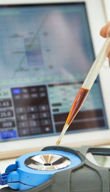 Hand using pipette with refractometer in front of tablet displaying measurement interface.