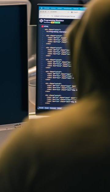 A person in a hoodie coding on dual monitors, depicting cybersecurity and hacking themes.